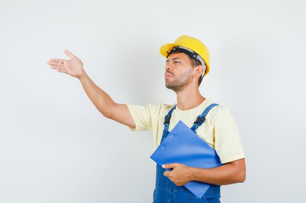 Joven ingeniero sosteniendo el portapapeles y dando instrucciones en vista frontal uniforme.