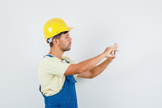 Joven ingeniero en uniforme tomando fotos en el teléfono móvil.