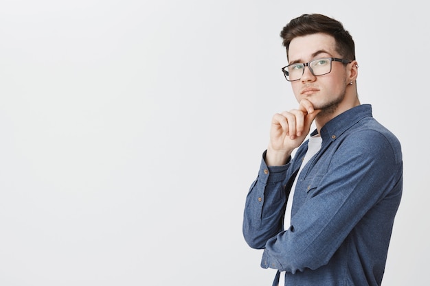 Joven inteligente con gafas mirando pensativo, reflexionando sobre la idea