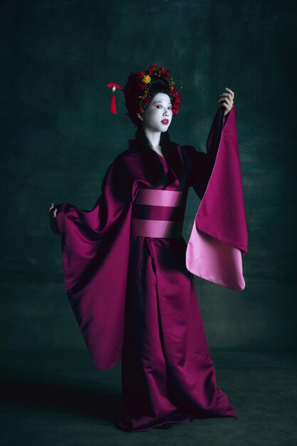 Joven japonesa como geisha en pared verde oscuro