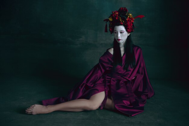 Joven japonesa como geisha en verde oscuro. Estilo retro, comparación del concepto de eras.