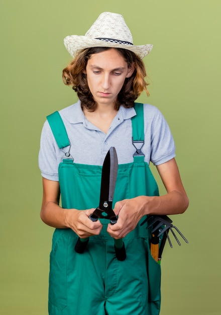 Foto gratuita joven jardinero hombre vestido con mono y sombrero sosteniendo cortasetos