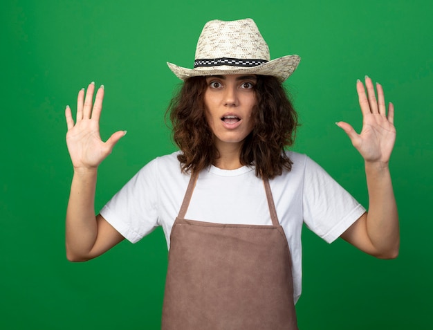 Joven jardinero sorprendido en uniforme vistiendo sombrero de jardinería extendiendo las manos