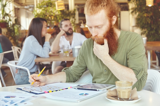 Joven jengibre con tableta en café