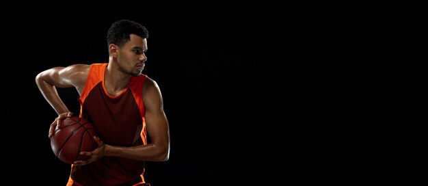 Joven jugador de baloncesto africano entrenando en estudio negro.