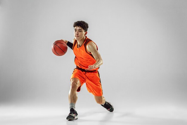 Joven jugador de baloncesto del equipo con entrenamiento de ropa deportiva, practicando en acción, movimiento en ejecución aislado en la pared blanca