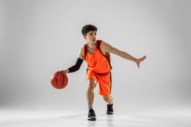 Joven jugador de baloncesto del equipo con entrenamiento de ropa deportiva, practicando en acción, movimiento en ejecución aislado en la pared blanca