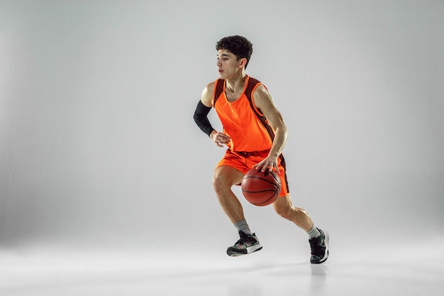 Foto gratuita joven jugador de baloncesto del equipo con entrenamiento de ropa deportiva, practicando en acción, movimiento en funcionamiento aislado en la pared blanca. concepto de deporte, movimiento, energía y estilo de vida dinámico y saludable.