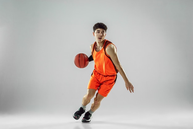 Joven jugador de baloncesto del equipo con entrenamiento de ropa deportiva, practicando en acción, movimiento en funcionamiento aislado en la pared blanca. Concepto de deporte, movimiento, energía y estilo de vida dinámico y saludable.