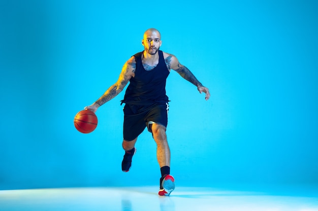 Joven jugador de baloncesto del equipo vistiendo ropa deportiva, practicando en acción, aislado en la pared azul en luz de neón