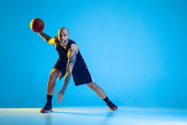 Joven jugador de baloncesto del equipo vistiendo ropa deportiva, practicando en acción, aislado en la pared azul en luz de neón