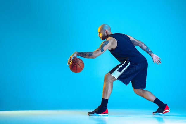 Joven jugador de baloncesto del equipo vistiendo ropa deportiva, practicando en acción, aislado en la pared azul en luz de neón