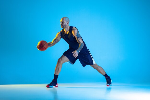 Joven jugador de baloncesto del equipo vistiendo ropa deportiva, practicando en acción, aislado en la pared azul en luz de neón