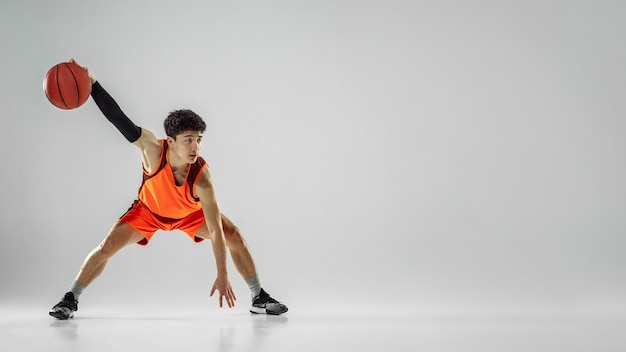 Foto gratuita joven jugador de baloncesto del equipo vistiendo ropa deportiva, practicando en acción, movimiento en marcha aislado sobre fondo blanco.