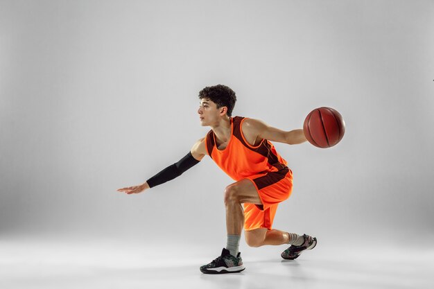 Joven jugador de baloncesto del equipo vistiendo ropa deportiva, practicando en acción, movimiento en marcha aislado sobre fondo blanco.