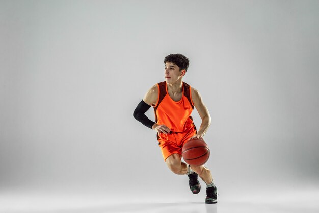 Joven jugador de baloncesto del equipo vistiendo ropa deportiva, practicando en acción, movimiento en marcha aislado sobre fondo blanco.