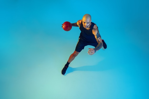 Joven jugador de baloncesto del equipo vistiendo ropa deportiva, practicando en acción, movimiento en la pared azul con luz de neón