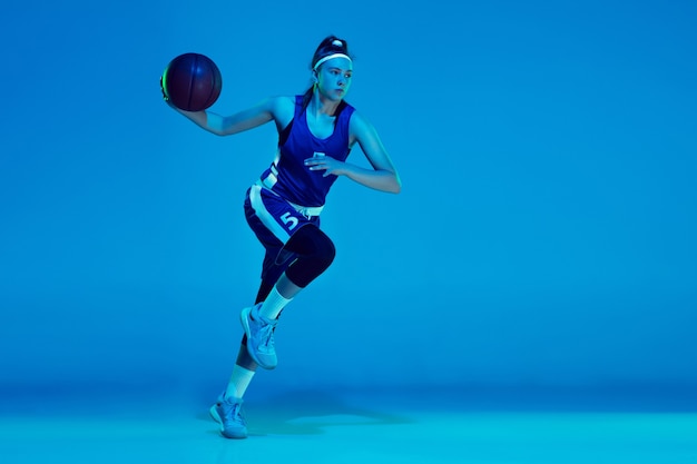 Joven jugador de baloncesto femenino caucásico aislado en estudio azul en luz de neón