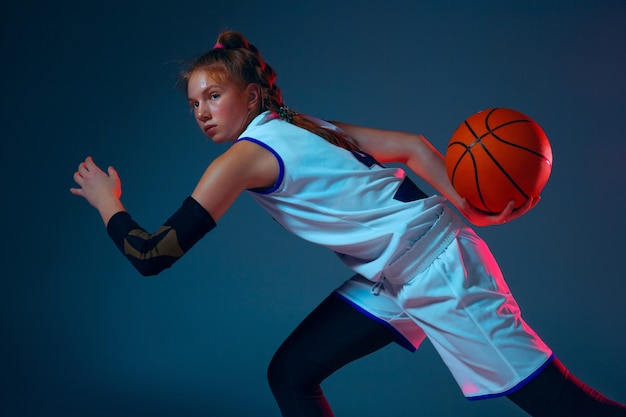 Joven jugador de baloncesto femenino caucásico en la pared azul en luz de neón