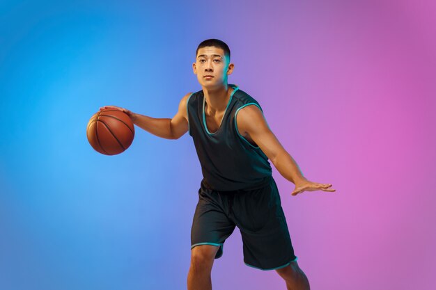 Joven jugador de baloncesto en movimiento sobre fondo de estudio degradado en luz de neón