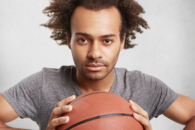 Joven jugador de baloncesto negro sostiene la bola, mira con confianza,