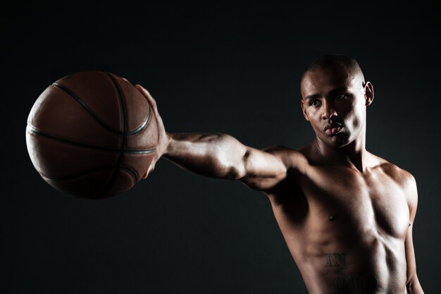 Joven jugador de baloncesto serio sosteniendo la pelota con una mano