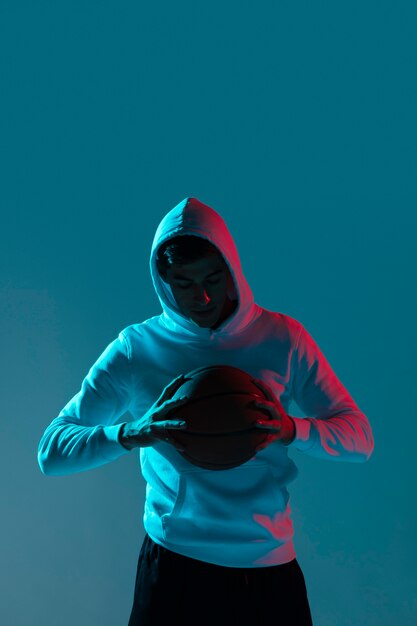 Joven jugando baloncesto solo con luces frías