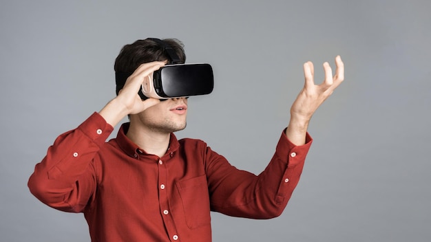 Foto gratuita un joven está jugando juegos usando gafas vr sosteniendo un fondo gris virtual