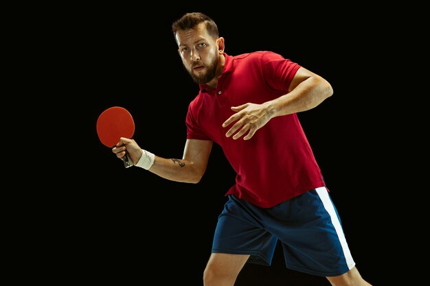 Joven jugando tenis de mesa en estudio negro