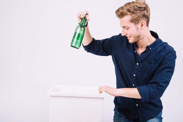 Joven lanzando botella verde en el cubo de basura