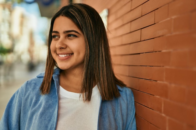 Joven latina sonriendo feliz de pie en la ciudad