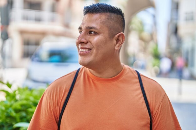 Joven latino sonriendo confiado mirando hacia un lado en la calle