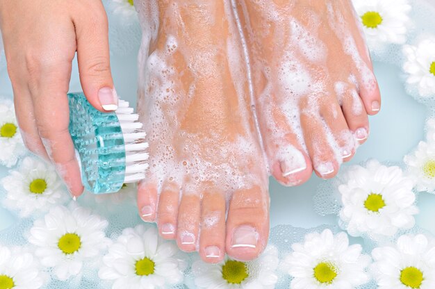 La joven lava y limpia las hermosas piernas bien arregladas con agua mediante un cepillo de limpieza.