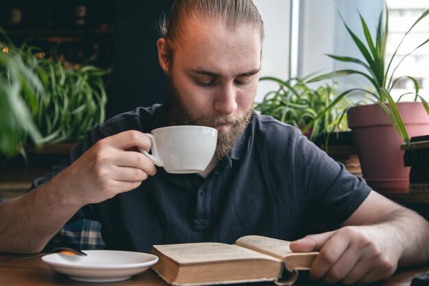 Un joven lee un libro con una taza de té en un café.