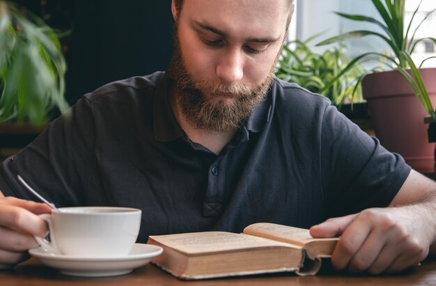 Un joven lee un libro con una taza de té en un café.