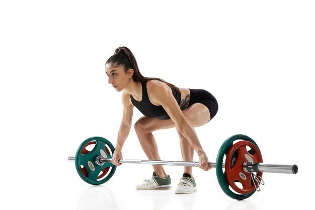 Un joven levantador de pesas femenino fuerte entrena con una barra de peso aislada sobre fondo blanco Concepto de levantamiento de pesas deportivo