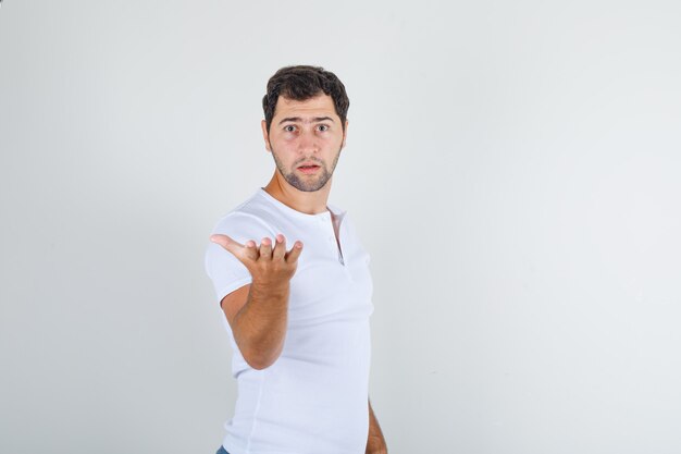 Joven levantando el brazo en gesto de interrogación en camiseta blanca y mirando furioso