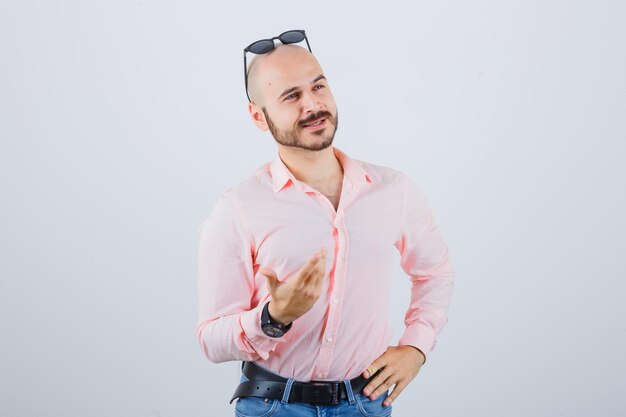 Joven levantando la mano mientras se habla de algo en camisa rosa, jeans, gafas de sol vista frontal.