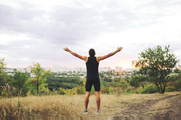 Joven levantando las manos sobre el cielo del atardecer después del entrenamiento