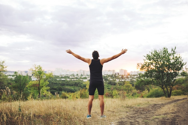 Joven levantando las manos sobre el cielo del atardecer después del entrenamiento