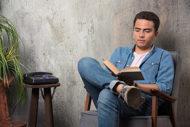 Joven leyendo un libro y sentado en una silla. Foto de alta calidad