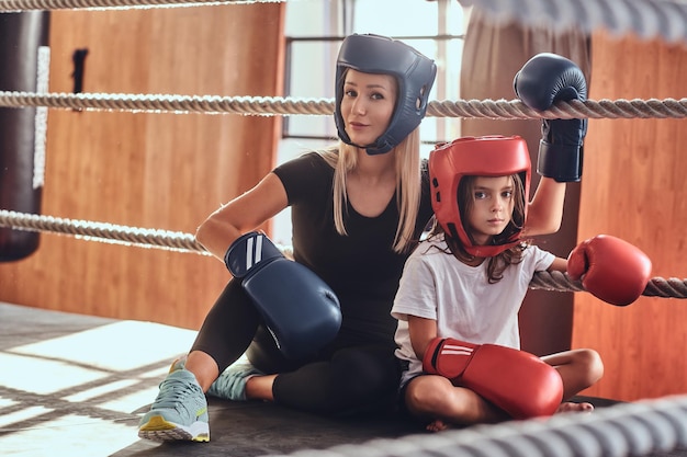 Una joven linda con casco y su hermosa entrenadora de boxeo están posando para el fotógrafo en el ring.