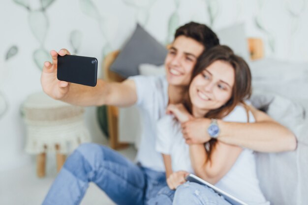 Una joven y linda pareja se fotografía a sí misma en su casa en la cabaña cerca de la cama.