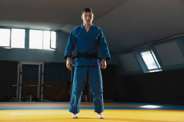 Un joven luchador en kimono entrenando artes marciales en el gimnasio