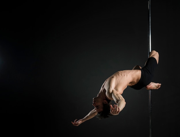 Joven macho fuerte realizando un pole dance