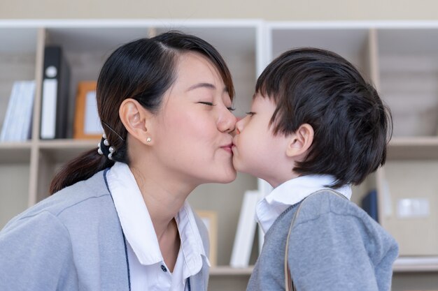 Joven madre alegre con niño besando su mejilla en el dormitorio