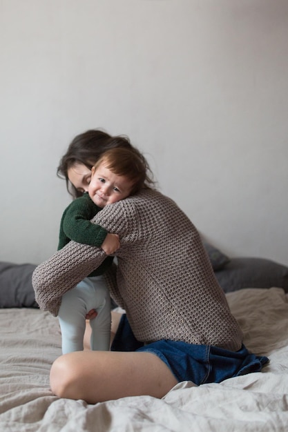 Foto gratuita joven madre y bebé en suéteres de punto jugando en el concepto de cama estilo de vida de confort en el hogar