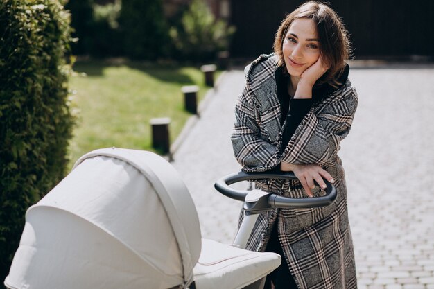 Joven madre caminando con carro de bebé en el parque