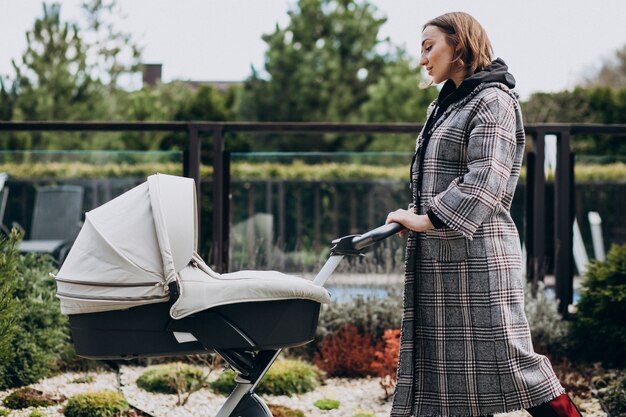 Joven madre caminando con carro de bebé en el parque