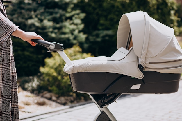 Foto gratuita joven madre caminando con carro de bebé en el parque